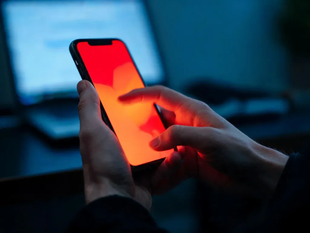 Zdenerwowane dłonie przewijają telefon z czerwono-pomarańczową poświatą, oddając emocjonalny charakter treści ragebait.